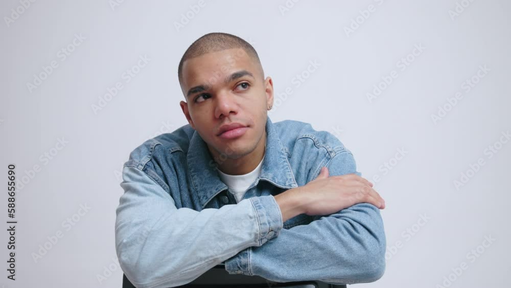 Fashion photoshoot concept. Bald male model in denim jacket looking straight to the camera with arms resting on top rail chair. High quality 4k footage Fashion photoshoot concept. Bald male model in denim jacket looking straight to the camera with arms resting on top rail chair. High quality 4k footage
