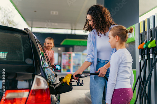 the mother fills the car with fuel at the gas station and talks to her daughters about the upcoming trip