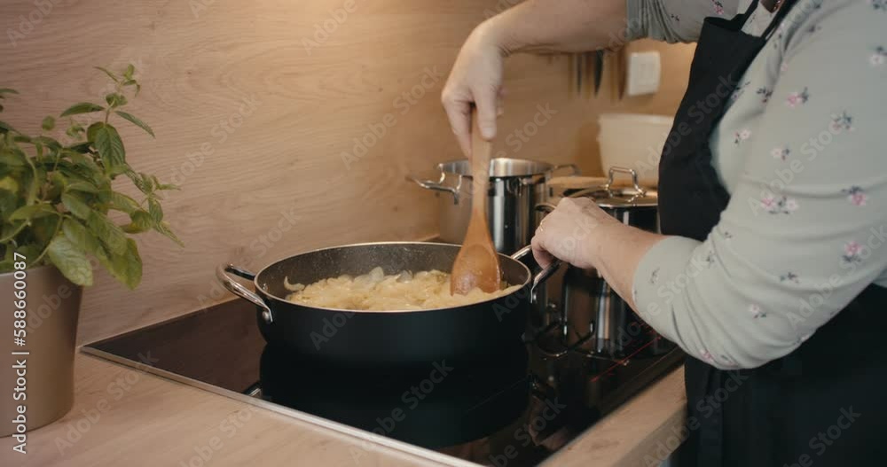Female cook hand spoon stirs onion frying in a pan kitchen close up Female cook hand spoon stirs onion frying in a pan kitchen close up