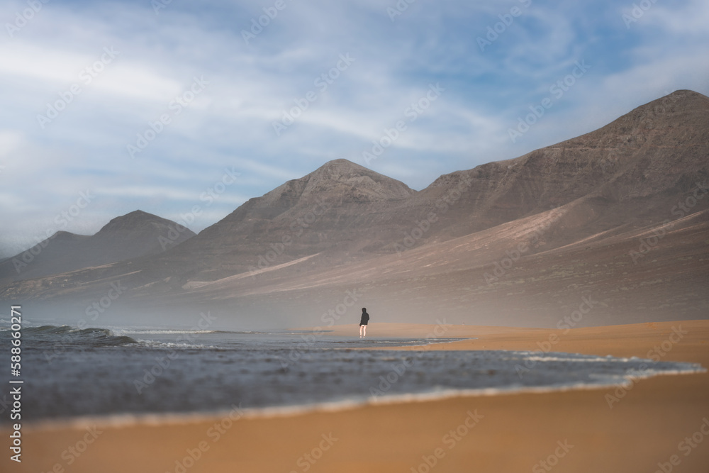 Stunning view a person walking on the Cofete beach surrounded by the chain of mountains of the Jandía Natural Park. Fuerteventura, Canary Islands. Stunning view a person walking on the Cofete beach surrounded by the chain of mountains of the Jandía Natural Park. Fuerteventura, Canary Islands.