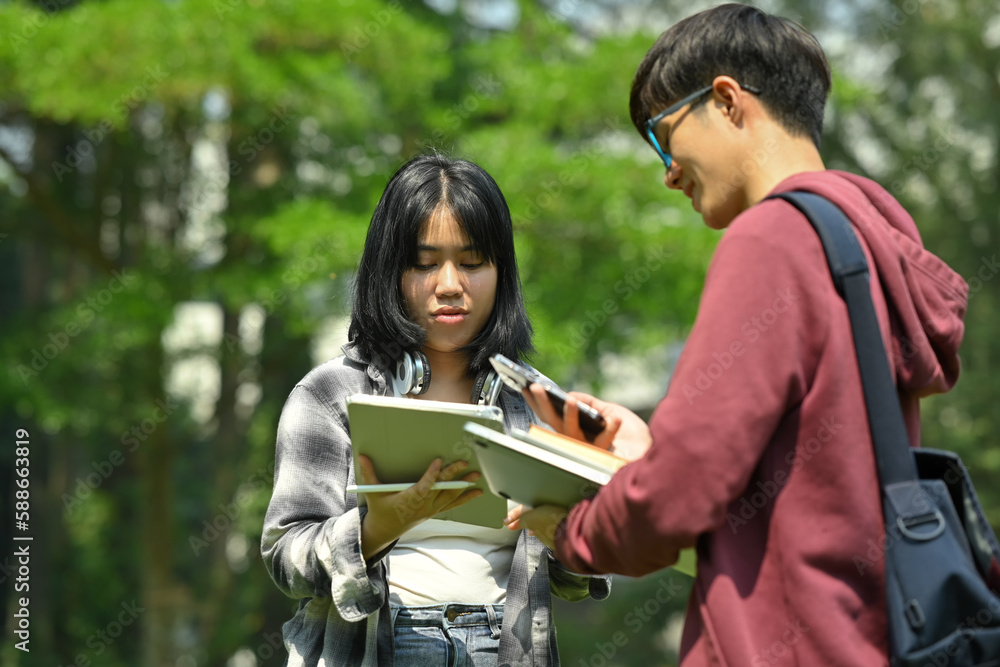 Two asian students are talking to each other after classes while walking outdoors in university. Education and youth lifestyle concept Two asian students are talking to each other after classes while walking outdoors in university. Education and youth lifestyle concept