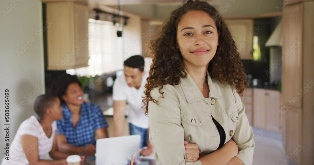 Happy biracial woman in kitchen and looking at camera with diverse friends in background Happy biracial woman in kitchen and looking at camera with diverse friends in background