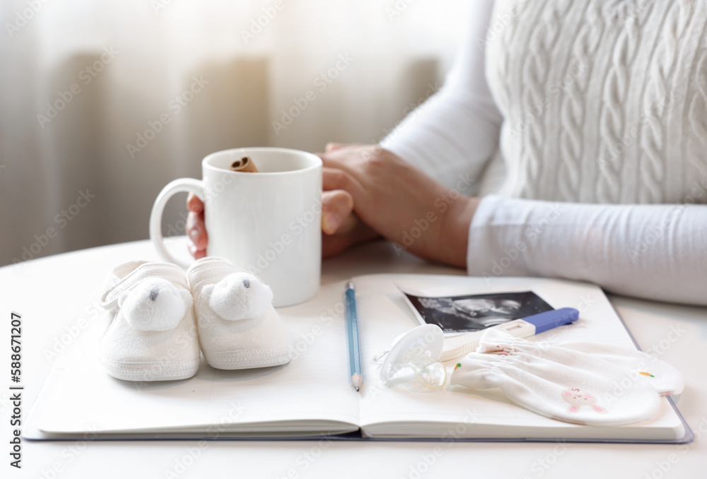 A pregnant woman is waiting leisurely with a teacup, notebooks and baby items are placed in front A pregnant woman is waiting leisurely with a teacup, notebooks and baby items are placed in front