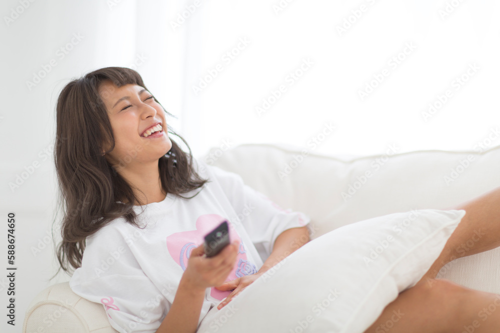 ソファーの上でリモコンを持って大笑いをする女性 ソファーの上でリモコンを持って大笑いをする女性