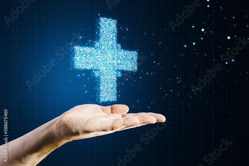 Close up of female hand holding creative glowing medical cross plus hologram on dark background. Healthcare and digital transformation concept.
