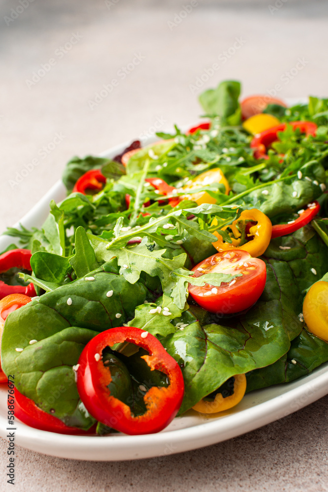 Salad of fresh farm vegetables in an oval dish on a pink background, sitya lettuce and chard, tomatoes and colorful bell peppers, arugula and sesame seeds Salad of fresh farm vegetables in an oval dish on a pink background, sitya lettuce and chard, tomatoes and colorful bell peppers, arugula and sesame seeds
