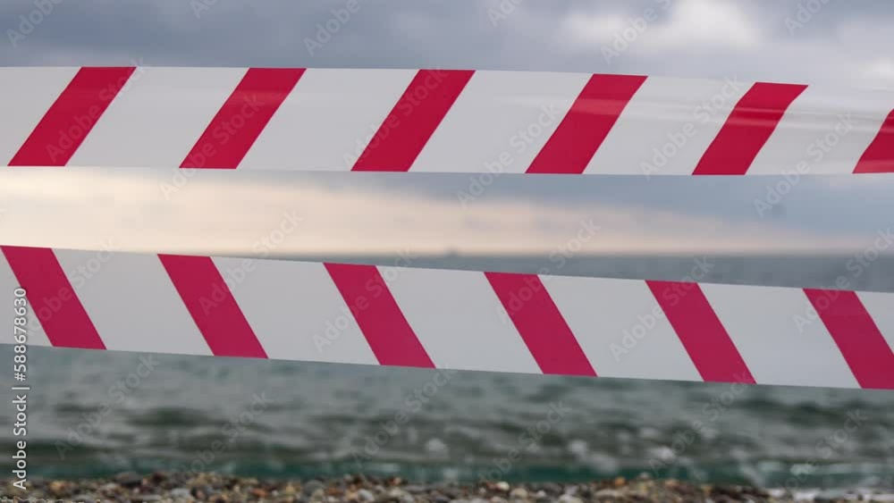 Red white warning tape barrier ribbon swinging in the wind across exotic sea beach background without people. No entry Red White caution tape. No holiday concept, delayed travel, no summer plans Red white warning tape barrier ribbon swinging in the wind across exotic sea beach background without people. No entry Red White caution tape. No holiday concept, delayed travel, no summer plans