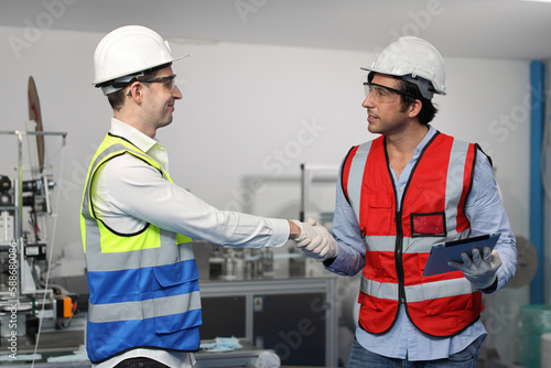 Caucasian mechanic technician maintenance, repairing industrial machinery equipment in factory. Worker in protective clothing with goggles and mask shaking hands greeting at manufacturing factory