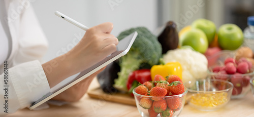 Panoramic of hand professional nutrition healthful surrounded by a variety of fresh fruits and vegetables working on digital tablet. Concept of right nutrition, diet and healthcare.