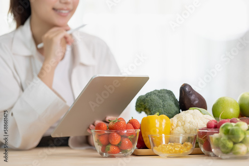 фотографія Close up hand of professional nutrition healthful surrounded by a variety of fresh fruits and vegetables working on digital tablet