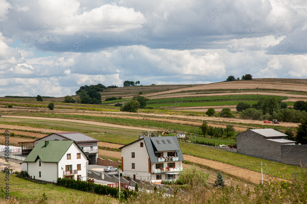 Farmland village. Rural scenery. Nature landscape. White cottage houses on meadow hills with harvest fields fluffy sky clouds daylight panorama.