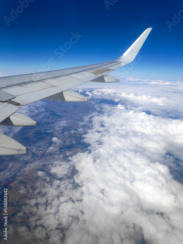 View from the window of the wing of an airplane flying above clouds and a blue sky.