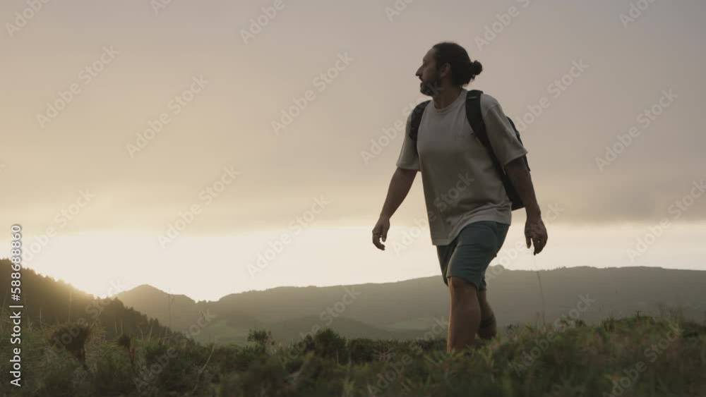Man with backpack hikes by storm clouds at the Azores, ground view pan Man with backpack hikes by storm clouds at the Azores, ground view pan