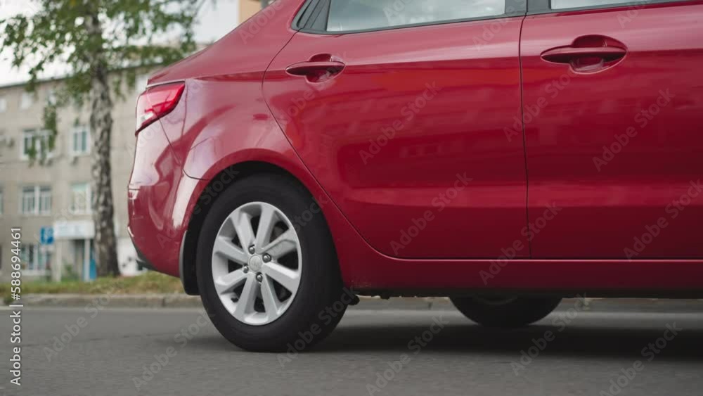 Red car sedan drives on empty street passing old buildings on sunny summer day. Elegant classy automobile moves on asphalt road in town closeup