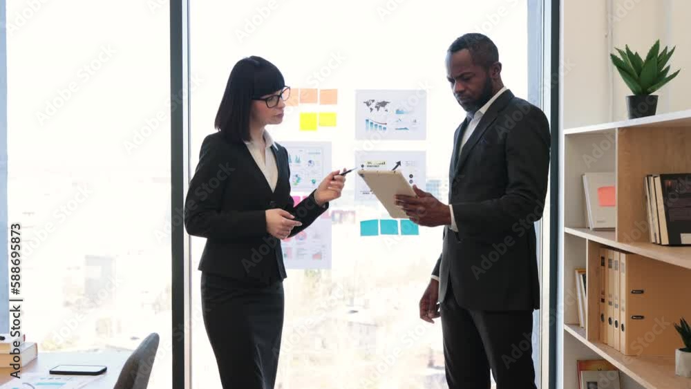 Caucasian woman and multiracial man in formal attire discussing graphs and charts in creative workplace. Competent businesspeople brainstorming about new project while meeting in conference room. Caucasian woman and multiracial man in formal attire discussing graphs and charts in creative workplace. Competent businesspeople brainstorming about new project while meeting in conference room.