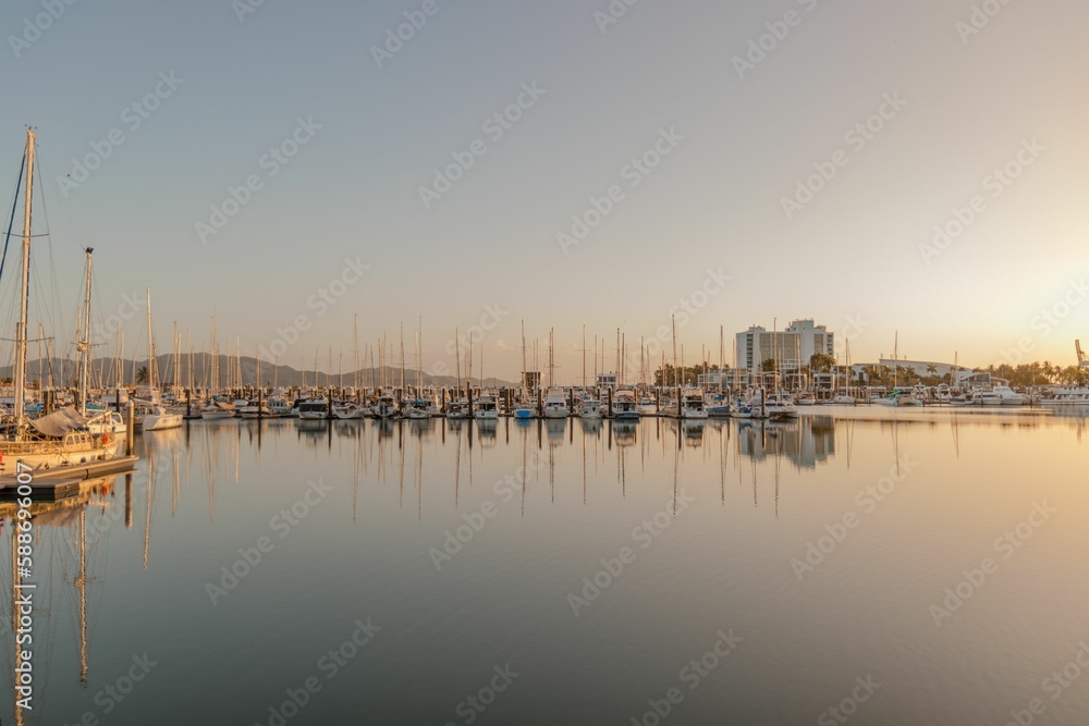 Row of boats in the harbor of a city reflected on the surface of the water at sunrise