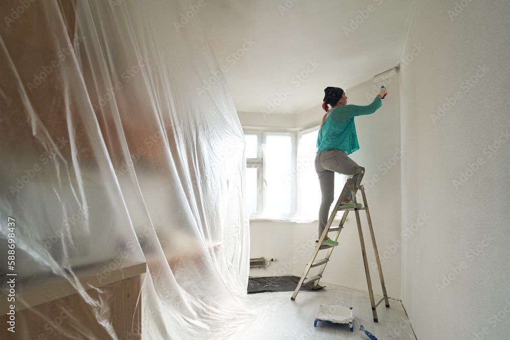 Woman stands on the stairs and paints the wall with a roller