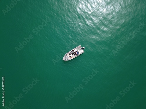 Aerial top view of a boat sailing in a tranquil lake on a sunny day © Tactisquatch/Wirestock Creators