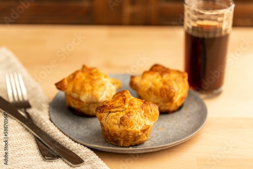 High-angle view of three kouign-amanns in the gray plate and a glass of drink over the wooden table