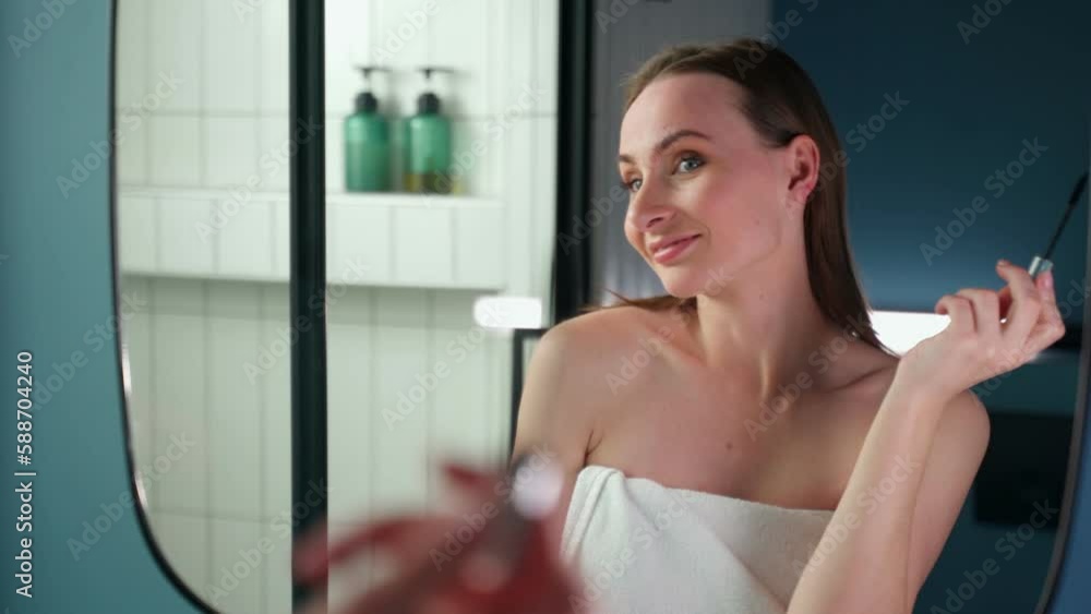 An attractive young woman paints her eyelashes with mascara in front of the bathroom mirror