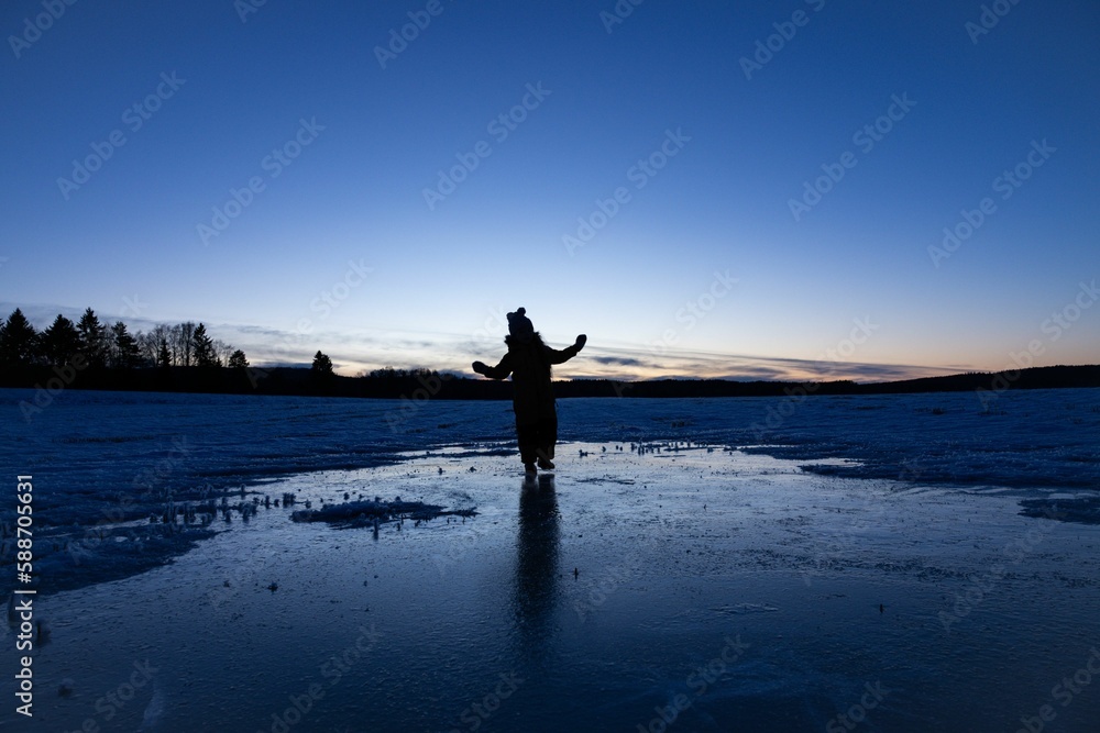 Fototapeta premium Silhouette of a young kid standing on the ice in the mountains in winter