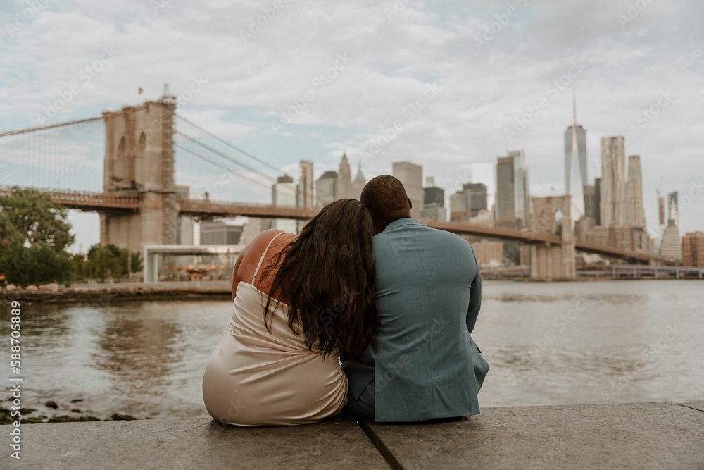 Back view of a couple sitting by the river and looking at the New York skyscrapers