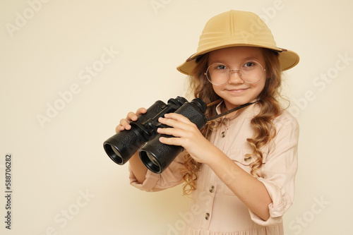 Traveler child. Child discoverer. Young researcher. Little girl in a safari hat with binoculars in her hands. Concept: search for adventure and treasure. Cute happy girl in safari clothes