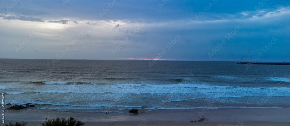 Panoramic shot of a wavy sea and people surfing near the beach at sunrise