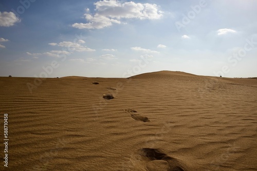 Scenic view of large footprints in the desert with sand dunes under blue cloudy sky