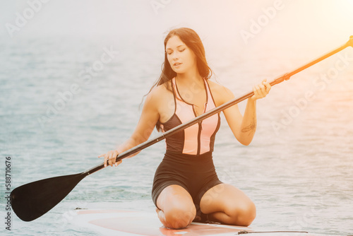 Close up shot of beautiful young caucasian woman with black hair and freckles looking at camera and smiling. Cute woman portrait in a pink bikini posing on sup board in the sea