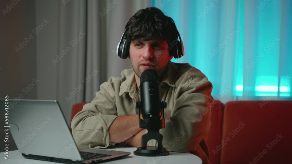 Happy young male audio blogger in headphones with laptop computer and microphone broadcasting at home office. Happy young male audio blogger in headphones with laptop computer and microphone broadcasting at home office.