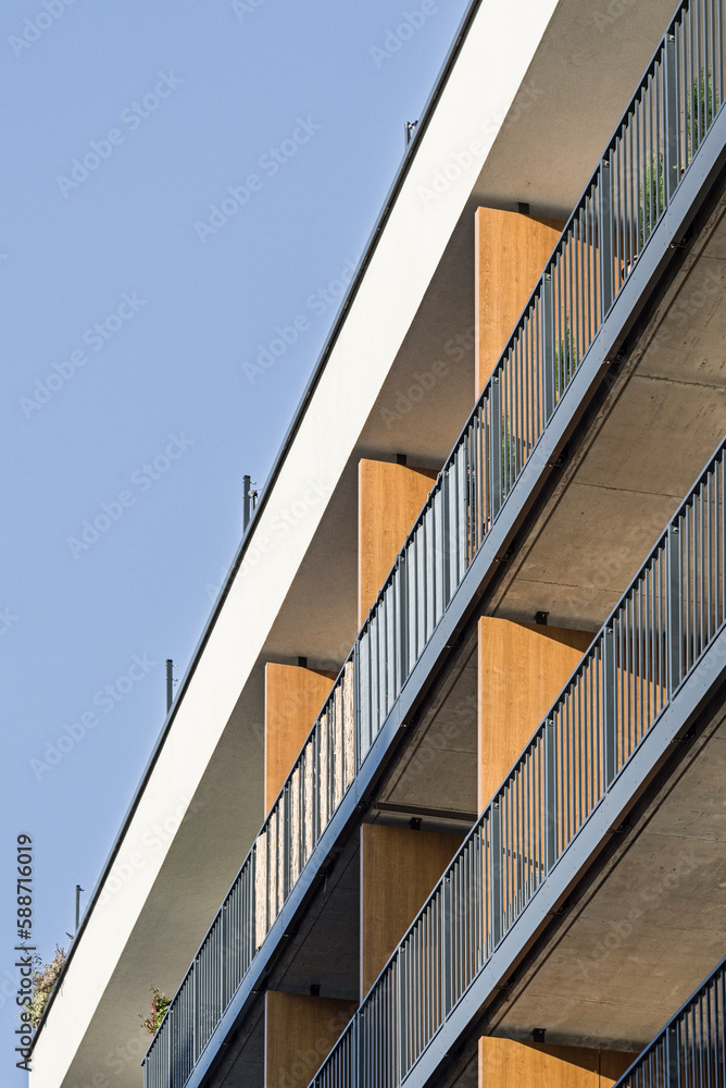 Fototapeta premium Detal na budynek wielorodzinny w centrum miasta. Duża ilość kondygnacji. Balkony i loggie. Duża ilość zieleni dookoła obiektu. 