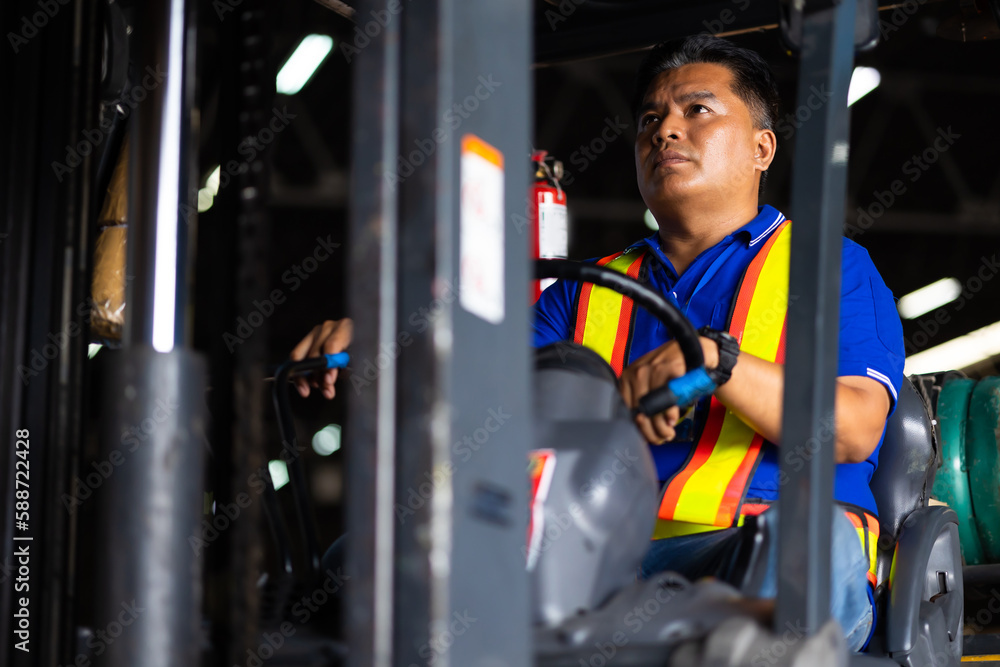 Asian man warehouse worker drive forklift in warehouse. Warehouse staff worker by goods shelf working in large warehouse factory Asian man warehouse worker drive forklift in warehouse. Warehouse staff worker by goods shelf working in large warehouse factory