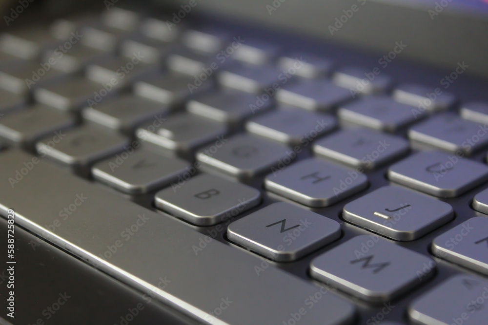 Closeup shot of a laptop gray keyboard with black colour font on black background, selective focus.