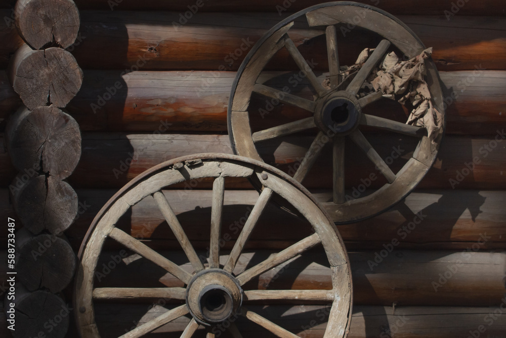 an old, authentic, wooden cart wheel against a vintage brown wall.