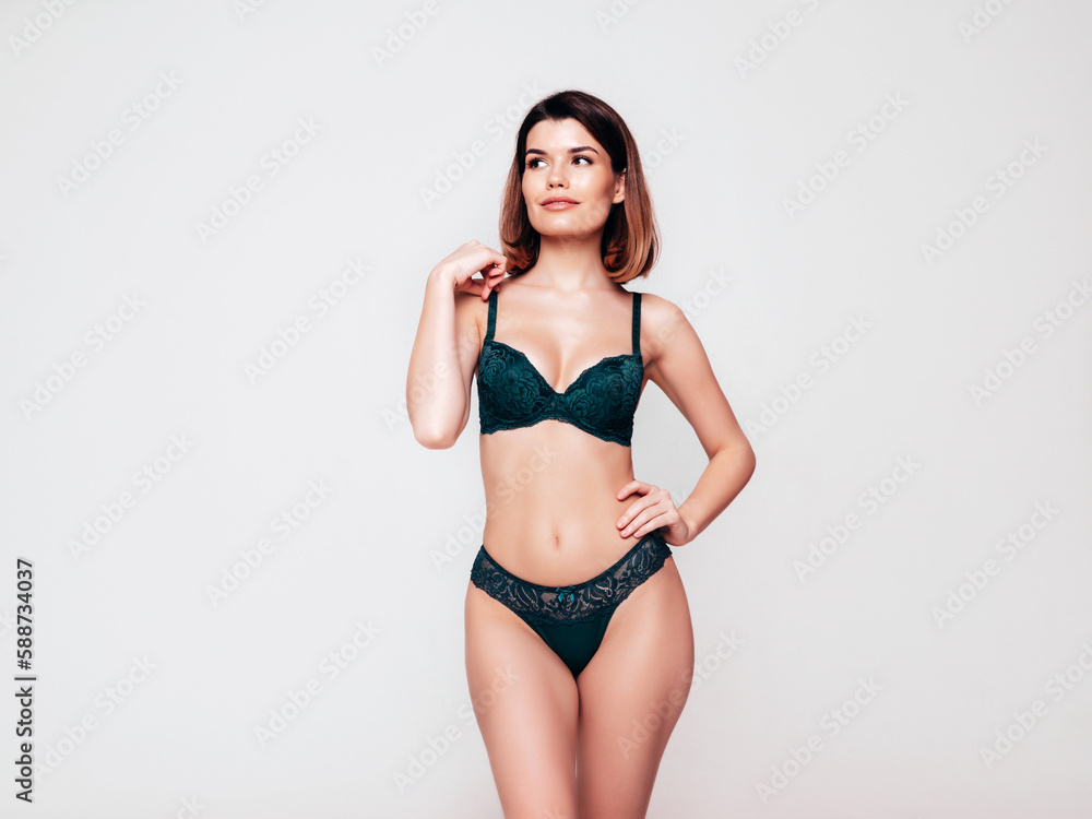 Young beautiful sexy woman in green lace lingerie. Carefree confident model wearing green underwear. Hot brunette posing on white wall in studio. Perfect body. Slim and fit. Isolated