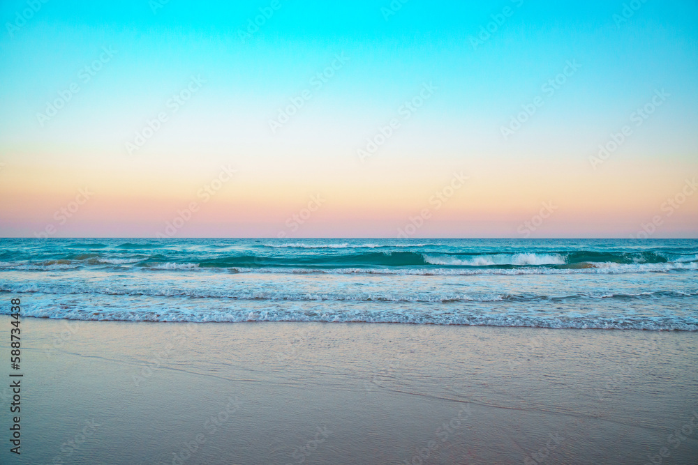 Mesmerizing sunrise over Pacific ocean and beautiful turquoise waves rolling in on a pristine sandy beach. 