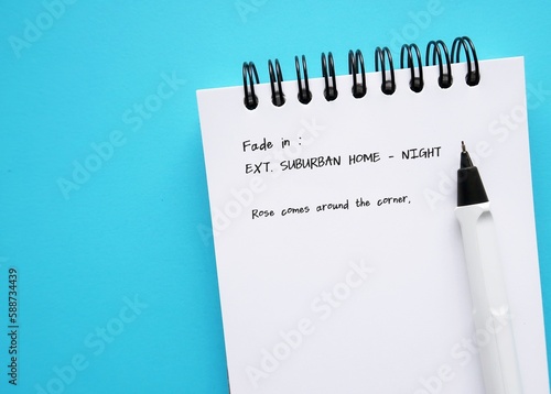 Pen and  notebook with screenwriting scene written, on blue copy space background.  Concept of  professional screenwriter job, TV or movie film script writing or concept of writer's block photo