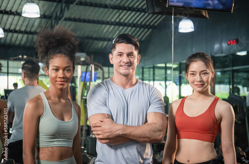 Young sports people and trainer in fitness gym  man with crossed hands and two women fit sporty  Sport and fitness concepts