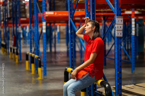 Tired hot wiping sweat. Warehouse female staff worker working hard standing by goods shelf in large warehouse factory.