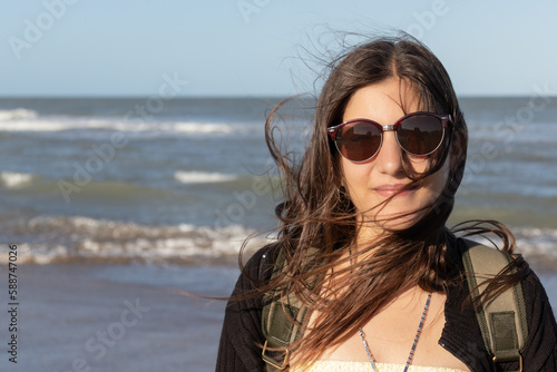 A beautiful young woman, around 25 years old, smiles with her white skin and brown hair blowing in the wind, wearing sunglasses and a yellow dress that shows her figure down to the middle of her body.
