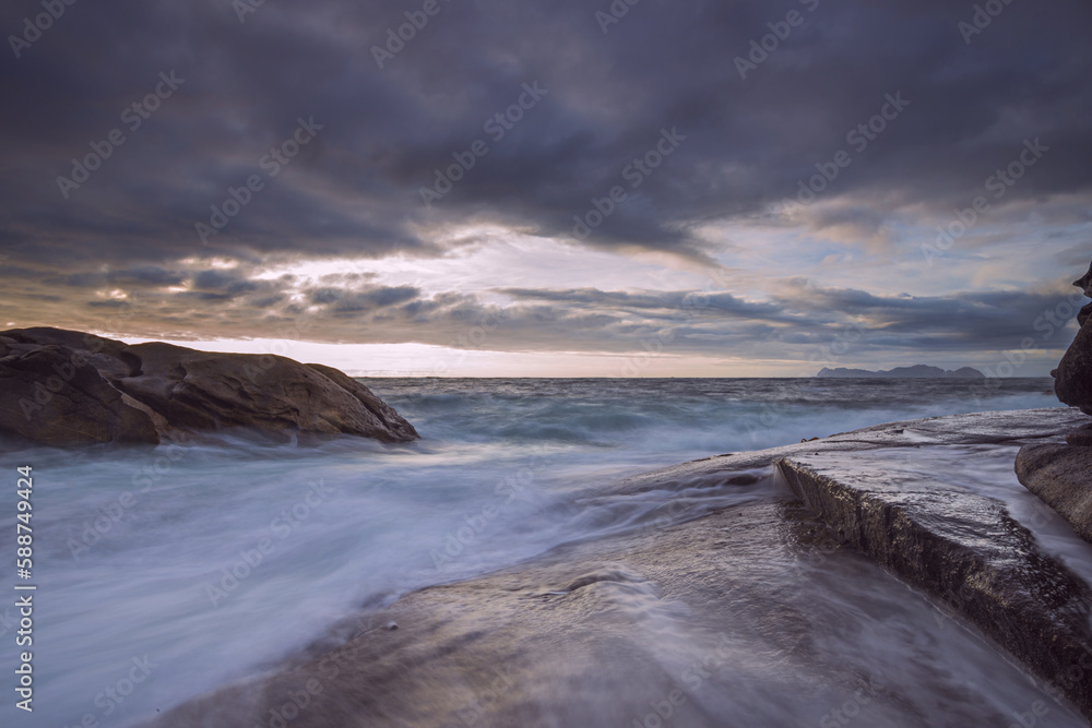 Fototapeta premium Long exposure image with waves shaking the reefs and forming a lot of foam at sunset on the Spanish Galician coast with the Cíes islands in the background