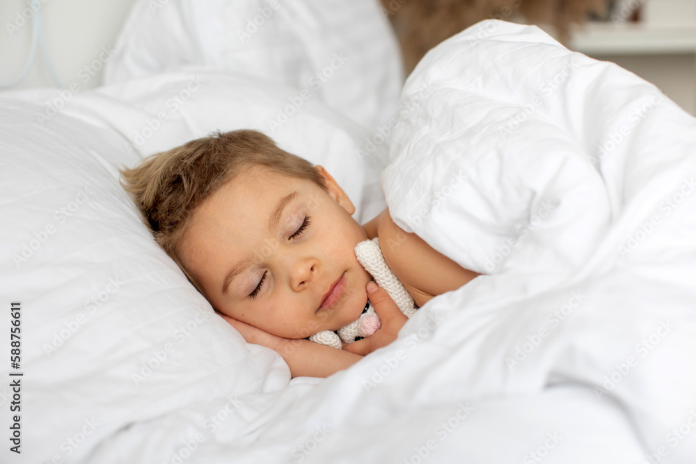 Beautiful blond toddler child, boy, sleeping in bed with teddy bear toy Beautiful blond toddler child, boy, sleeping in bed with teddy bear toy