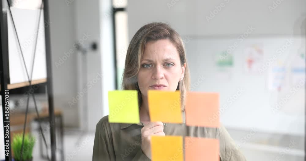 Thoughtful business woman working with paper note on glass wall. Finding new business solution and planning and sticky note on glass wall Thoughtful business woman working with paper note on glass wall. Finding new business solution and planning and sticky note on glass wall