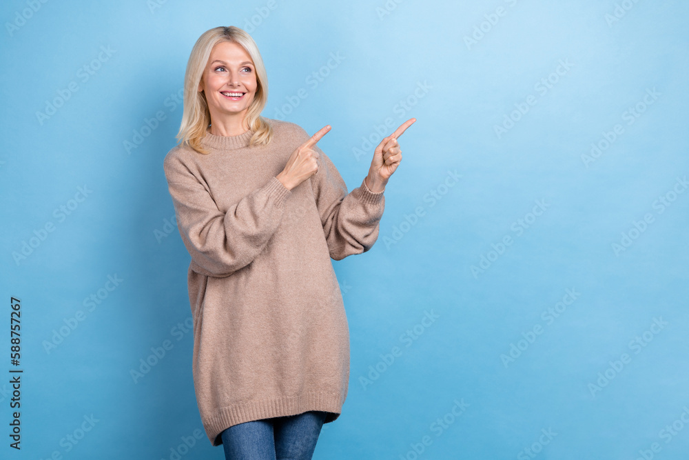 Photo of satisfied pensioner blonde hair woman wear beige long sweater direct finger mockup cheap clothes isolated on blue color background Photo of satisfied pensioner blonde hair woman wear beige long sweater direct finger mockup cheap clothes isolated on blue color background