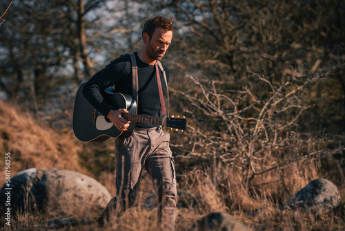 Man with an acoustic guitar is walking through the nature