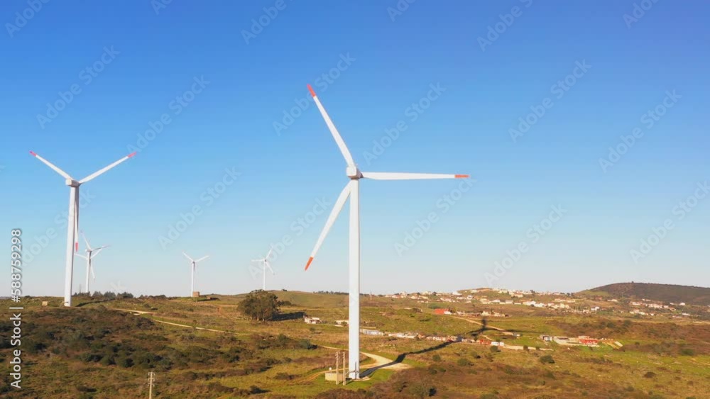 Wind turbines producing renewable source of energy on windfarm illuminated by sunlight. Windmills with rotor blades generating alternative electrical energy Wind turbines producing renewable source of energy on windfarm illuminated by sunlight. Windmills with rotor blades generating alternative electrical energy