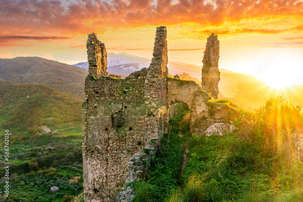 immersive landscape of old castle ruins on foreground and beautiful mountains with sunset with clouds on background