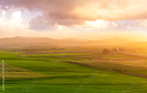 beautiful green valley with green fields with green spring grass with nive hills and mountains and scrnic colorful cloudy sunset on background of landscape