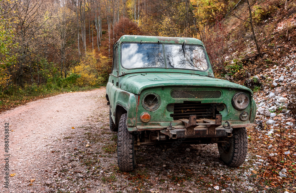 An old shabby terrain car on a rural road. A battered cark is parked on an old dirt road in a high-altitude forested area